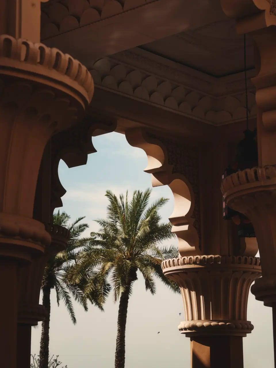 Traditional carved arches framing palms in a sunlit courtyard